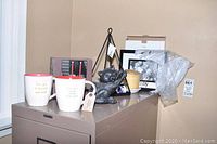 Two ceramic mugs, heavy metal cat door stopper, black metal candle holder, small wood candle holder, family photo frame on filing cabinet.