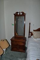 Full view of wooden side table with tall attached mirror against wall near bed and lamp