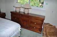 Long wooden dresser under window with six drawers and a central cupboard, brass handles, visible wear and scratches on surface.