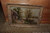 Front view of the framed oil painting showing a cottage, a woman feeding ducks beside a water body, in an ornate carved frame.