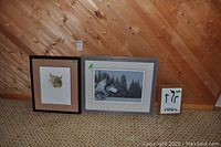 Three framed prints placed on wooden floor against wood paneled wall: Canadian Lynx print, wolf print, and Aboriginal art print.