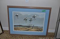 Framed print showing five swans flying over a marsh with some distant landscape features.