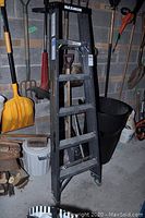 Photo of 6-foot aluminum Maximum ladder standing among various tools in a garage or basement setting, showing wear and use.