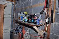 Wide view of items on a shelf including bottles of car care products, gas cans, extension cords hanging underneath, and a car brush on the wall.