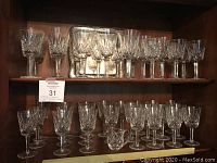 Two-tier wooden shelf displaying full set of assorted Waterford Lismore stemware pieces.