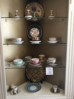 Display cabinet with glass shelves featuring assorted marked and unmarked china tea cups and saucers with decorative plates and candle holders.