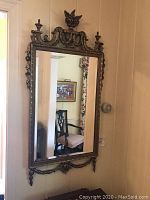 Front view of the ornate gold-leaf rectangular beveled mirror hanging on a wall in a hallway.