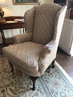 Front angle view of the wing back chair showing the diamond patterned upholstery and curved wood legs; visible wear on the arm.