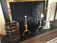 Full view of fireplace with brass andirons, tool stand with tools, and cylindrical firewood container placed on hearth