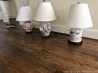 Photo showing all four table lamps lined up on wooden floor with white pleated shades.