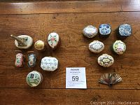 Overview of 14 pill/trinket boxes and a fan-shaped pin on a wood table
