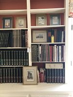 Photograph showing small framed prints and photographs of historic landmarks on upper shelves, with multiple travel, art, and reference books below on shelves.