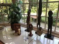 Photo of Schlabaugh & Sons mantle clock, three African wood carvings, copper pot, candle holder, and small carved wooden figure on a white tabletop near window