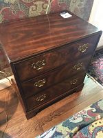 Front view of wooden chest showing three drawers with ornate brass handles, polished wood finish and slight wear on edges and base