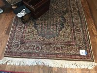 Overhead view of the full rug laid out on hardwood floor with fringe visible and furniture at one end.