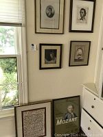 Six framed music themed prints and artwork on a wall and floor, showing a grouping of portraits and musical note sheets.