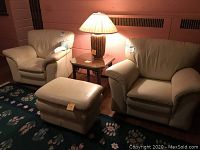 Two white leather chairs, one matching white leather ottoman, octagonal wooden side table, and table lamp with woven base and pleated shade. All items sit on a floral patterned rug.