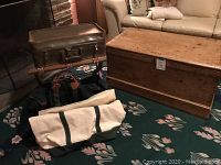 Photo showing wood trunk, luggage rack with leather straps, and four bags including brown leather suitcase, black duffel, green/tan tote, and beige/green canvas bag.