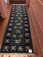 Hallway view of green runner showing full length, floral pattern and fringe.