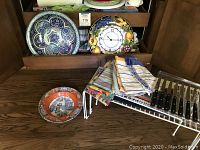 Photo showing three ceramic bowls and an Italian decorative wall clock along with assorted linens and a metal rack holding steak knives.