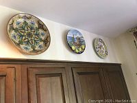 View of three ceramic plates and bowls displayed on a wall above cabinetry, showing variety in design and size.