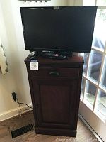 Full view of the wooden TV stand cabinet with 24" RCA TV on top, showing overall condition and remote on cabinet.