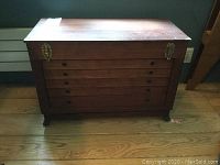 Front view of wooden storage chest showing 5 horizontal pull-out drawers with keyholes and two metal latches on the top lid.