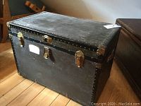 Old storage trunk black exterior with metal reinforced riveted edges, latch locks on front, and overall condition.
