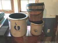 Two beige crocks and small wooden barrel atop a chest near window showing their relative size and condition.