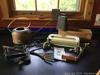 Overview of metal and wood items on a black table in front of a window, including a watering can, cowbell, mailbox decor, and vintage tools