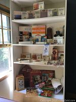 Shelf filled with various dollhouse miniature kits and books. Multiple titles visible on books and boxes.