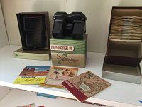 View of Sawyer's View-Master stereoscope viewer on its original box and light attachment in box with booklet catalogs laid out on shelf.