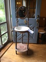 Full view of antique wooden wash stand with porcelain basin, wooden turned legs, base shelf, and upright supports with candle holders.