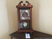 Full view of wooden decorative Wangja clock with brass pendulum and winding key placed in front on a table.