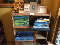 Books displayed on a wooden shelf showing multiple travel books including 'The Boswells Coast', 'Alaska' and various others in stacks.