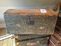 View of the entire wooden trunk showing the domed top with worn green paint and front forged lock plate with keyhole but no key.