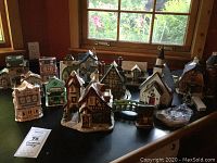 Front view of 14 Christmas village buildings arranged on a table beneath a window highlighting variety and snow details.