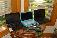 Three laptops arranged on a round wooden table alongside two power adapters and cables