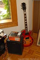 Full view of BC Rich guitar leaning against wall beside amplifier with Boss pedal box on top