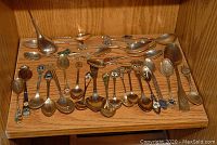 Photo showing multiple souvenir spoons laid out on a wooden surface, showcasing a variety of sizes and decorative patterns including enamel accents and metalwork.