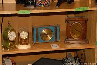 Shelf with four mantle clocks including Seth Thomas wooden clock and others, displaying their size in relation to shelf labels.
