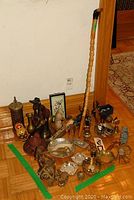 Various brass and wooden figurines, decorative bowls, large brass key, wooden cane and other decorative collectibles arranged on wooden floor