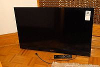 Front view of Sony TV leaning on floor showing screen and included remote.