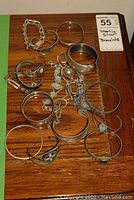 Assorted sterling silver bracelets and bangles laid out on wooden surface including curb chain, smooth bangles, wire loops, and wide cuff