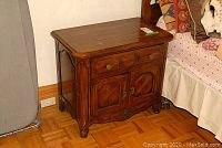 First wooden night stand showing front and side with drawer and door storage area, carved details and metal knobs.