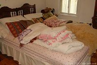 Bed covered with assorted folded linens and blankets including a white crochet afghan and other patterned blankets