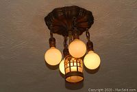 Photo of the vintage bronze ceiling light fixture mounted on the ceiling with four exposed bulbs and one bulb enclosed in a decorative glass globe.
