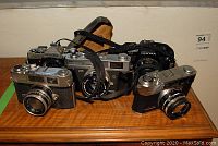 Overview of the five vintage 35mm cameras arranged on a wooden surface with shoulder strap attached to one camera.