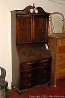 Front view of wooden china cabinet showing scrolled pediment, glass-paneled upper doors, and lower serpentine drawers