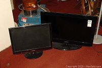 Two Samsung flat screen televisions of different sizes resting on carpet, front view showing screens and bases.